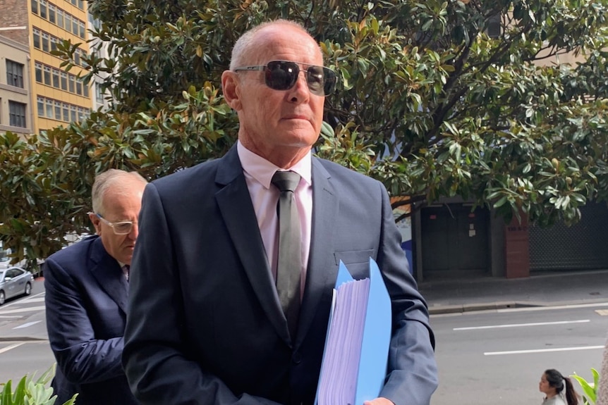 A man arriving at a court building in sunglasses and a suit.