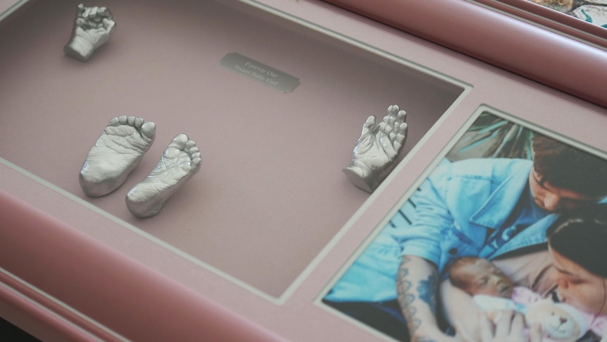 A close up of a pink picture frame with metal imprints of a baby's hands and feet. 