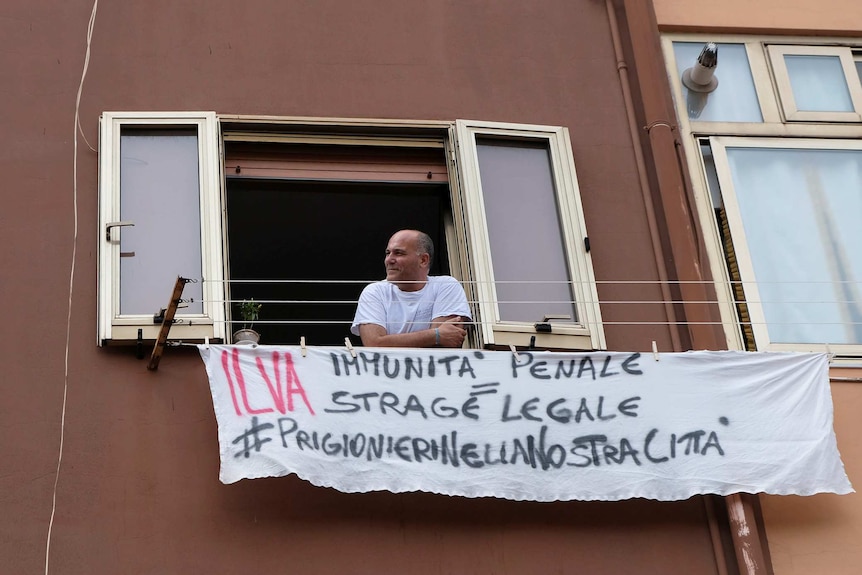 An Ilva worker hangs a sign reading "Ilva. Criminal impunity = legal massacre - Prisoners in our city".
