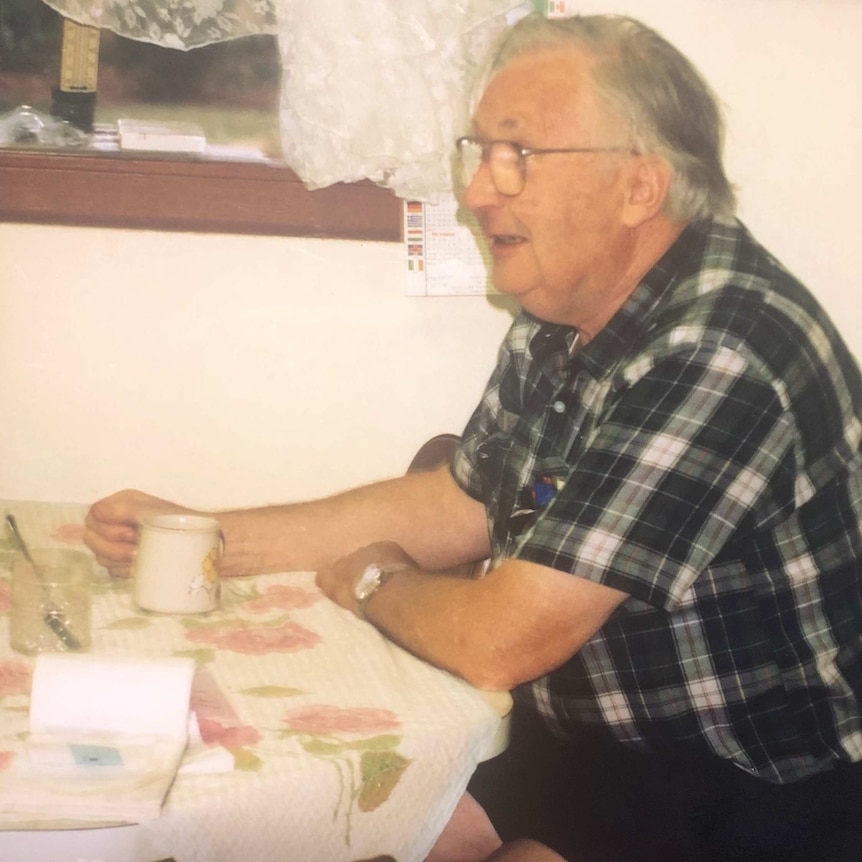 An older man sitting at a table with a coffee cup in his hand