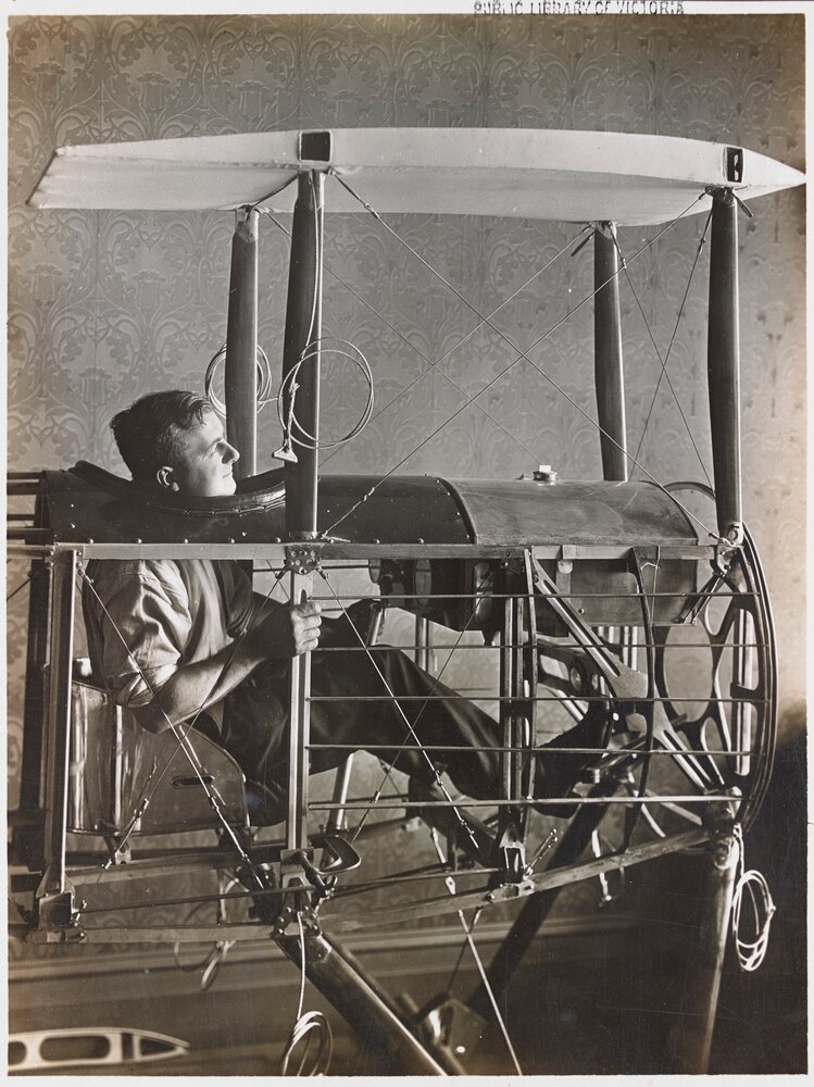 A young man sitting in the skeleton of a plane's cockpit, still under construction.