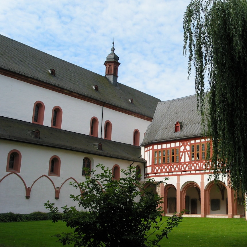 The outside of a medieval abbey with whitewashed walls and visible timber framing in lush green garden.