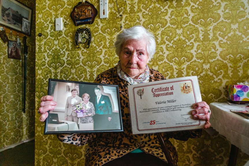 Valeria holds out photographs of people close to her and a certificate of appreciation for her volunteer work.