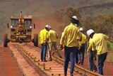 A crew in blue pants and yellow shirts work on a rail line with vehicle in background in the Pilbara