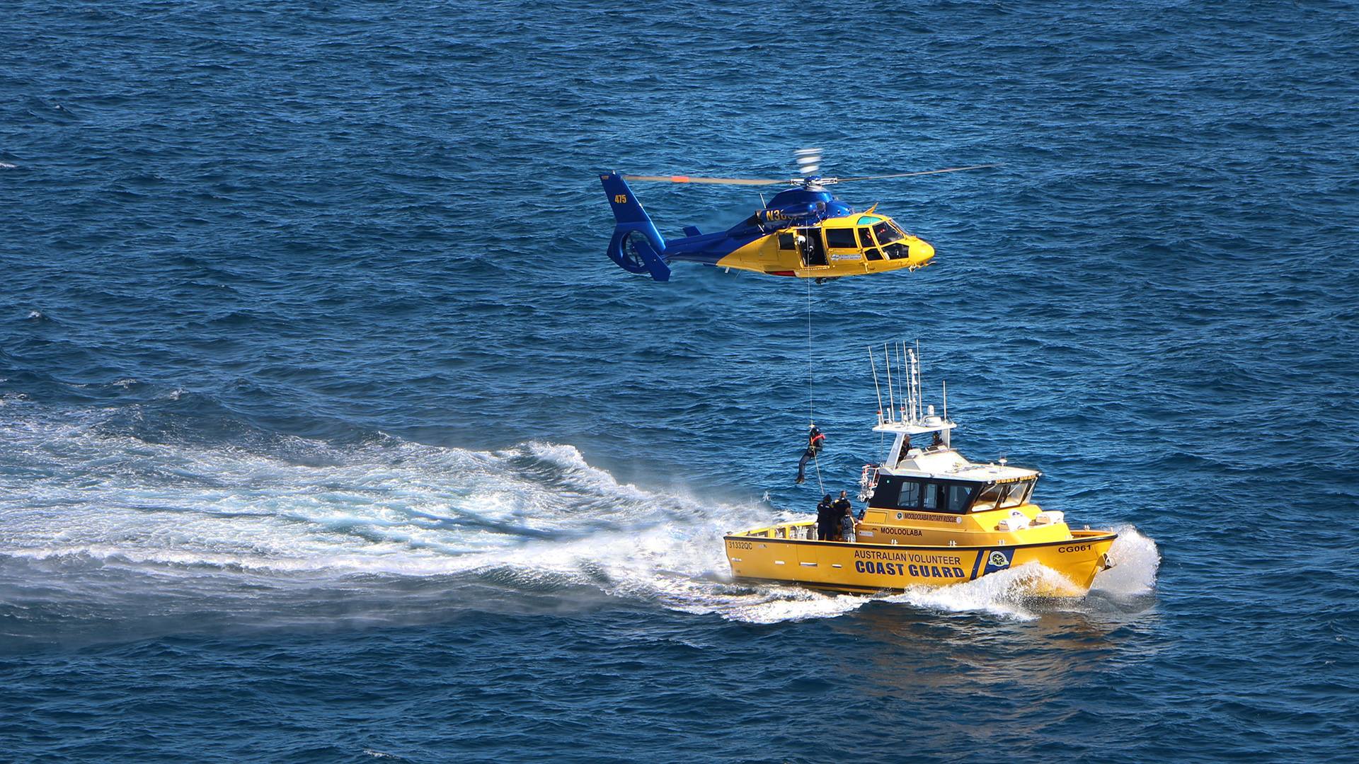Yellow rescue boat with rescue helicopter winching person down