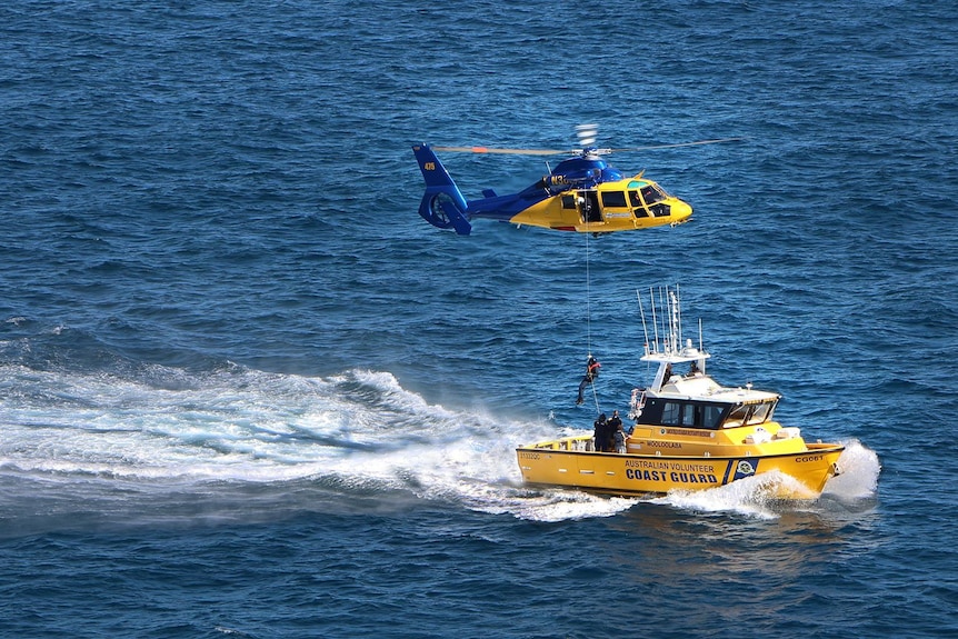 Yellow rescue boat with rescue helicopter winching person down
