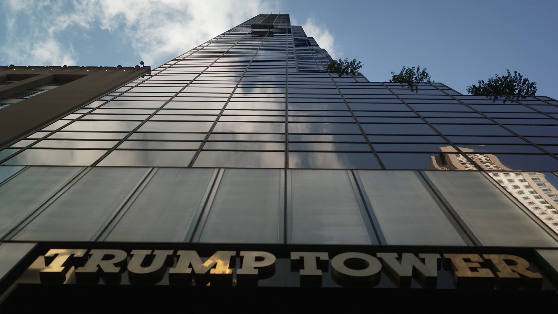 A view looking up at the Trump Tower skyscraper building in New York City on a sunny but cloudy day.