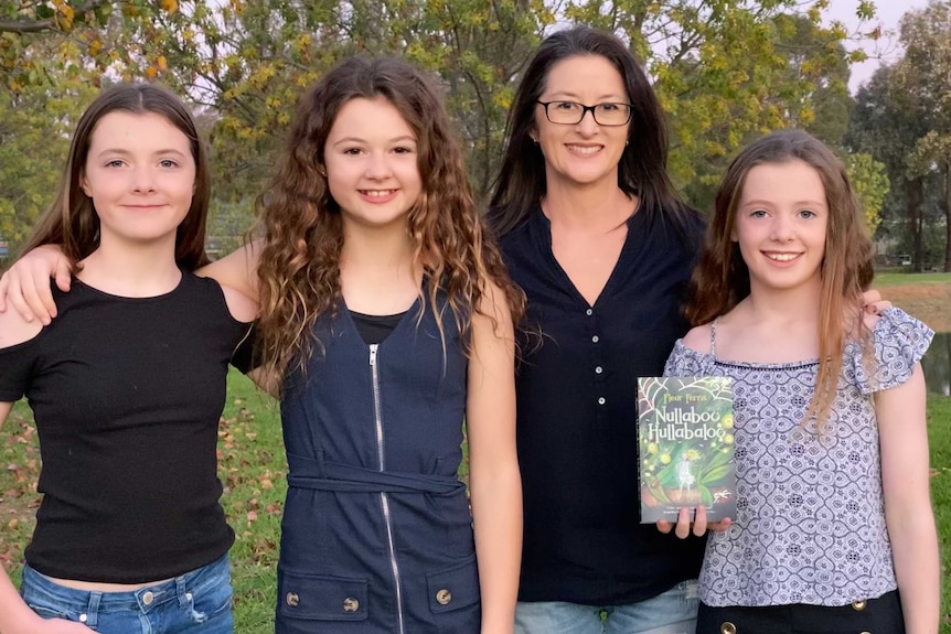 Female author standing with her three daughters holding her book