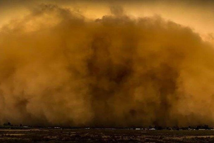 An orange and brown cloud of dust engulfs a town.