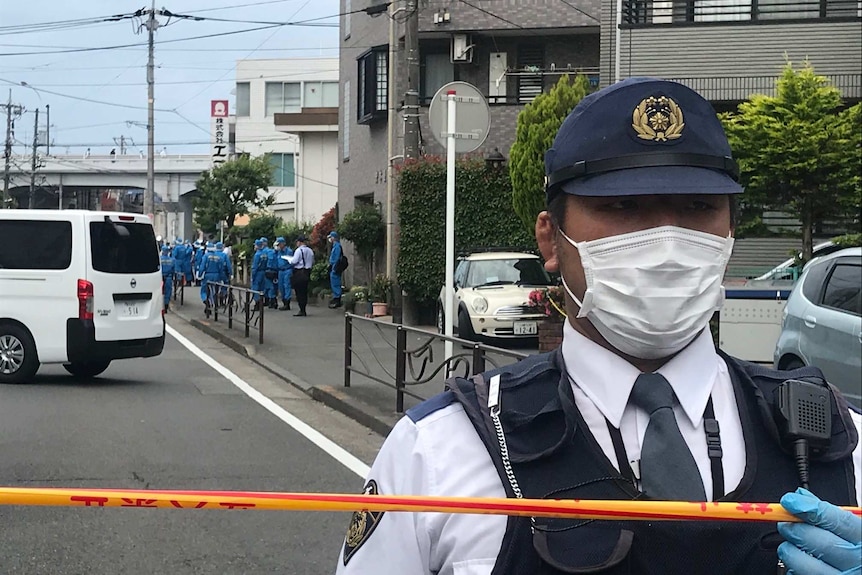 A policeman holds police tape with forensic investigators behind him