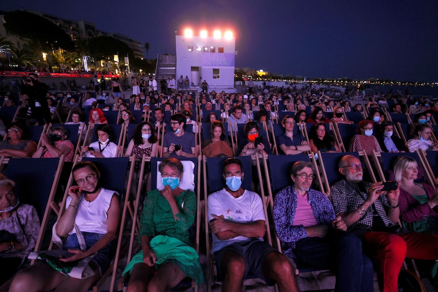 People sitting in rows, some wearing face masks. 