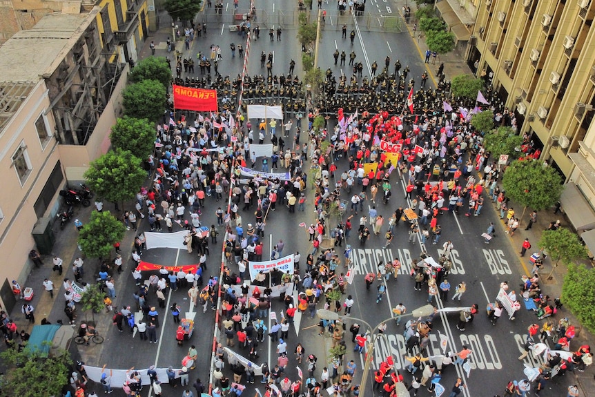 Вид сверху на протестующих, идущих по улице, вооруженных плакатами и плакатами полиции.