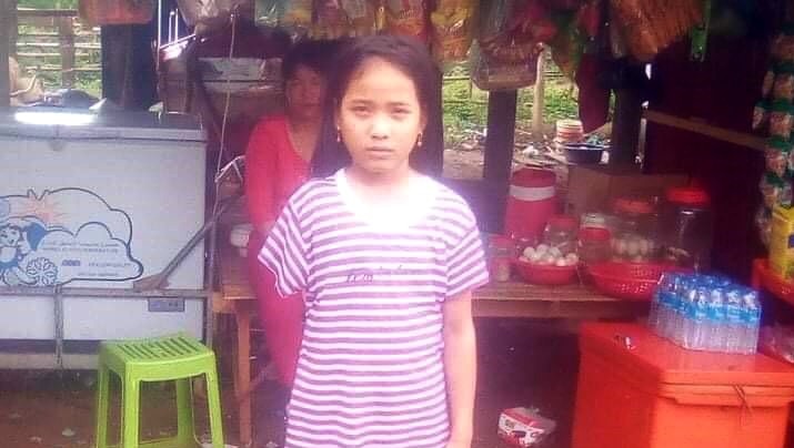 A girl stands in front of a Cambodian shop.