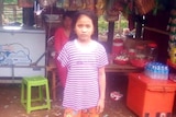 A girl stands in front of a Cambodian shop.