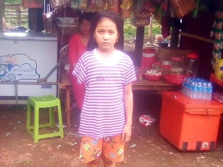 A girl stands in front of a Cambodian shop.
