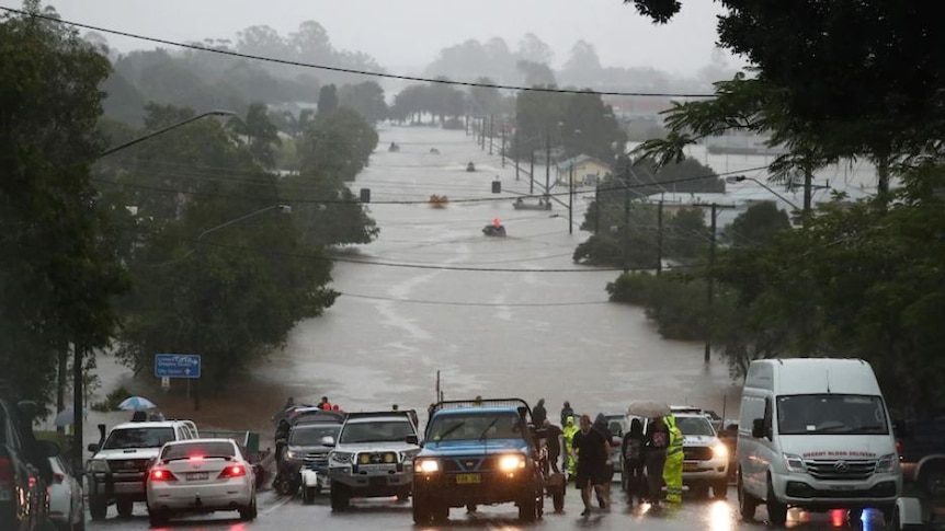 The view from a hill overlooking Lismore streets inundated by flood water. Vehicles are parked at the edge of the water.