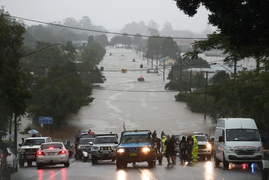 The view from a hill overlooking Lismore streets inundated by flood water. Vehicles are parked at the edge of the water.