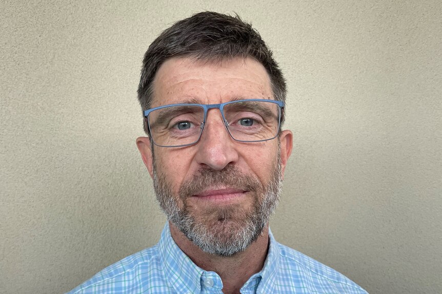 A man with a blue checked short, short beard and glasses