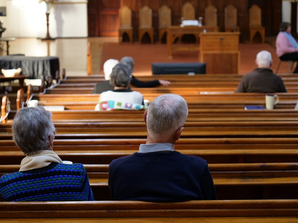 Six people spread out in the pews of a church, with their backs to the camera