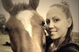 A woman poses with a horse and smiles at the camera