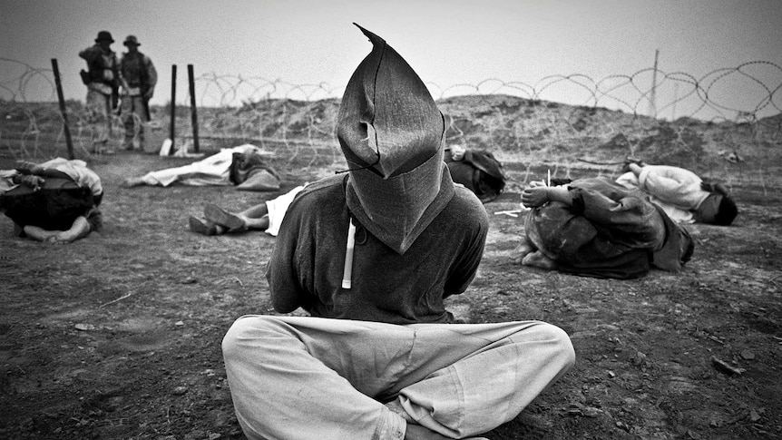 A Iraqi prisoner of war sits hooded surrounded by other POWs