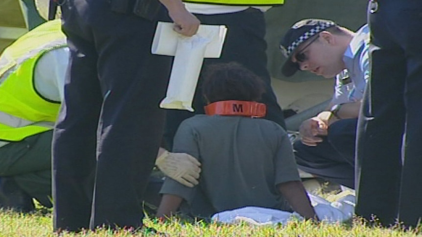 An Aboriginal boy sits on the ground after the fatal crash at Wilson, tended to by ambulance officers and police