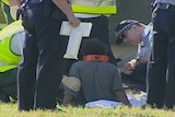 An Aboriginal boy sits on the ground after the fatal crash at Wilson, tended to by ambulance officers and police