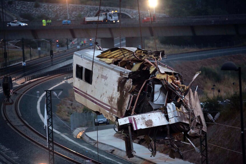 A crane lifts a mangled train carriage from the tracks