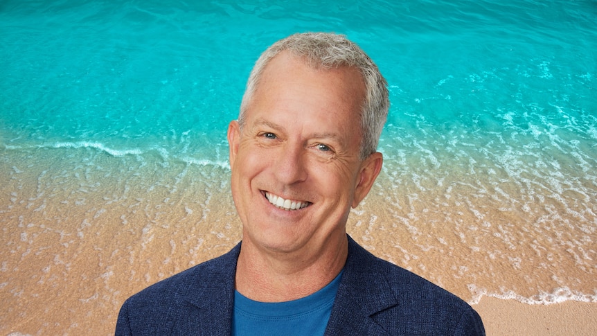 Breakfast presenter Mark Gibson smiling with image of beach sand and water behind him