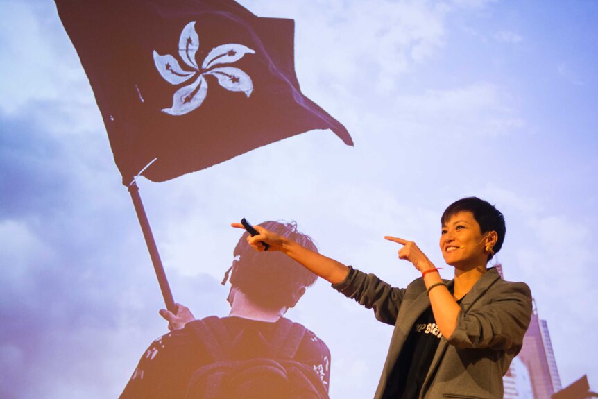 Denise Ho speaks in front of an image of a person waving a Hong Kong flag