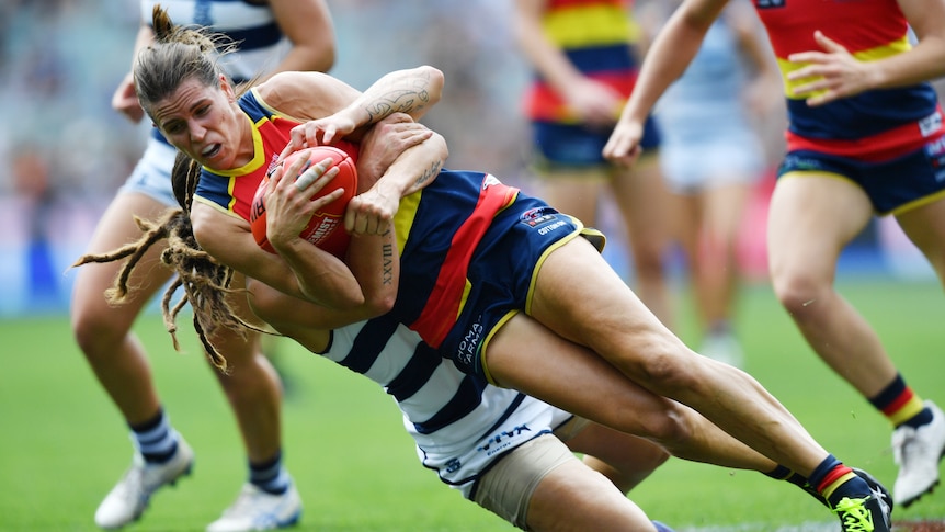 An Adelaide Crows AFLW player is tackled by a Geelong opponent.
