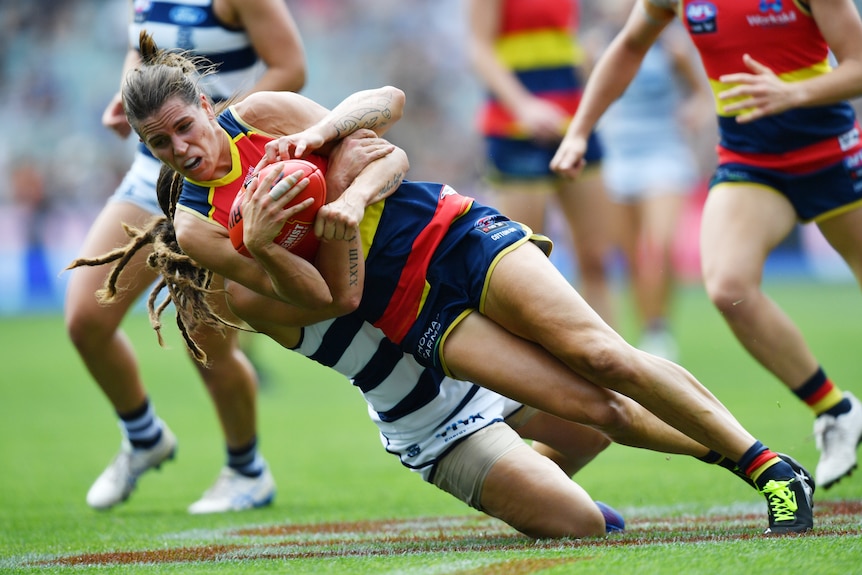 An Adelaide Crows AFLW player is tackled by a Geelong opponent.