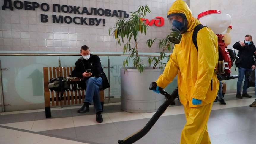 A cleaner in full body protective gear uses equipment to disinfect an open public area at a train station in Moscow.