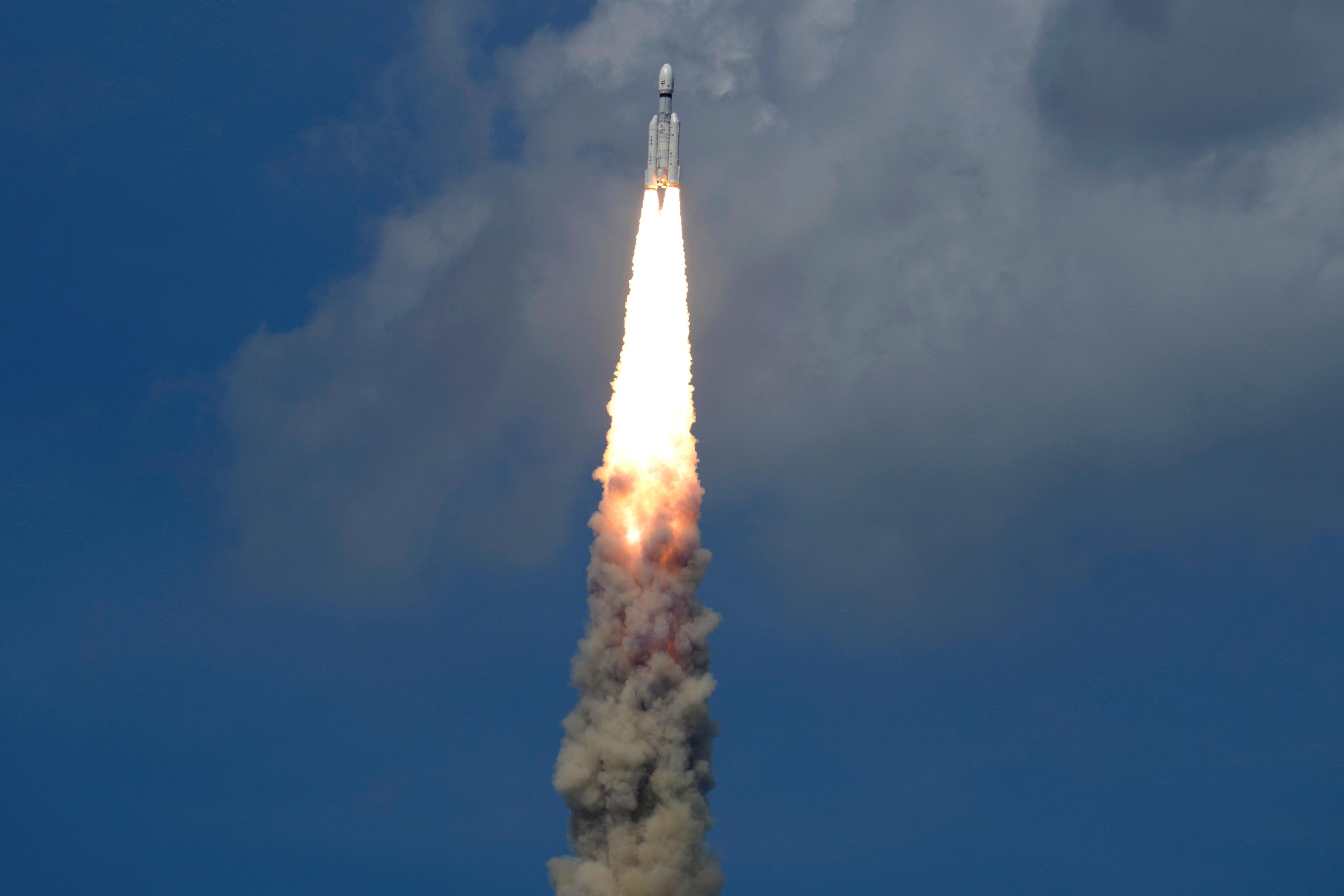 A large white space rocket leave a trail of flames and smoke as it flies into clouds and up into the sky.