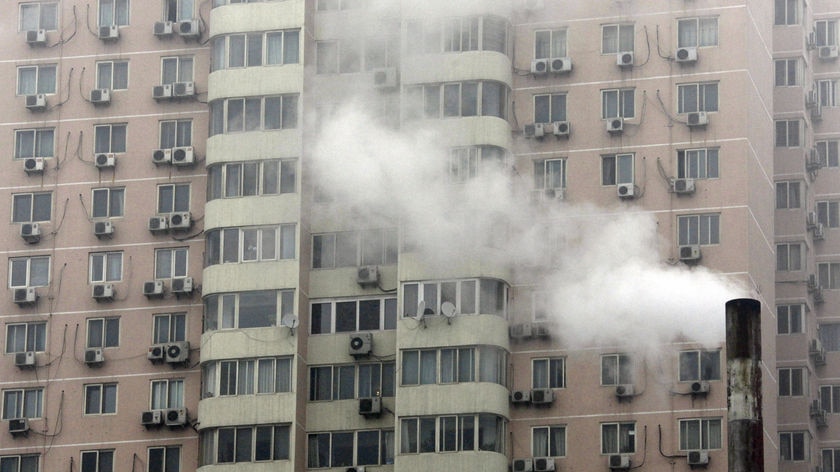 The facade of a large grey apartment block with a multitude of air conditioners under each window.