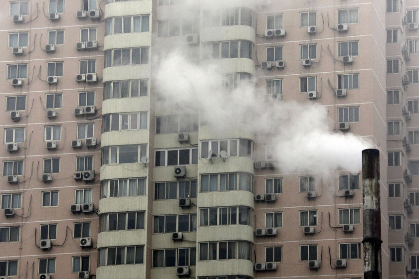 The facade of a large grey apartment block with a multitude of air conditioners under each window.