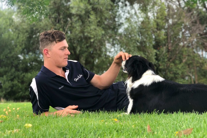 A young man lying on the grass with a black-and-white border collie