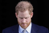 Prince Harry looks down as he fiddles with his jacket buttons while walking through a doorway.