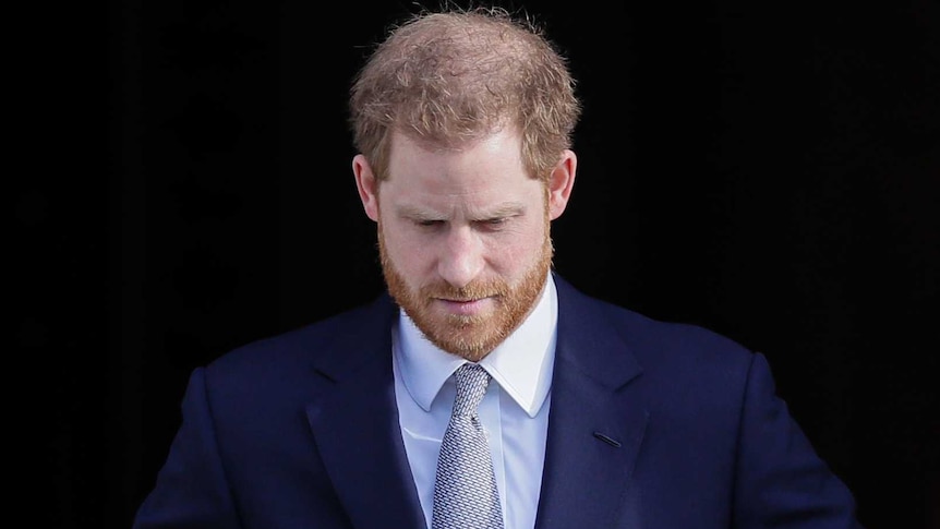 Il principe Harry guarda in basso, armeggiando con i bottoni della giacca, mentre attraversa la porta.