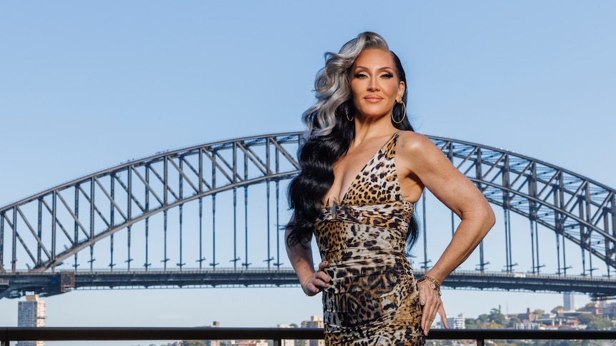 A woman is posing outside, in front of the Sydney Harbor Bridge