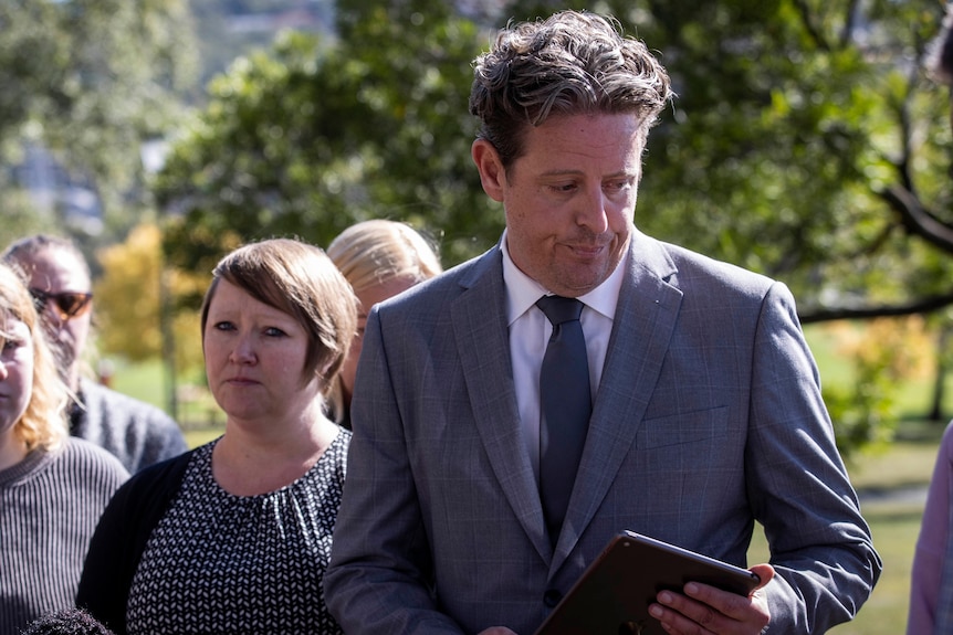 A man in a grey suit and his family stand in front of journalists.