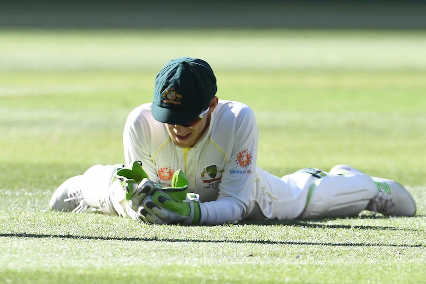 Australian wicketkeeper Tim Paine looks at his gloves while lying on the grass during a Test.