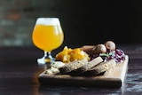 Bread, fruit and cheese on cutting board with beer