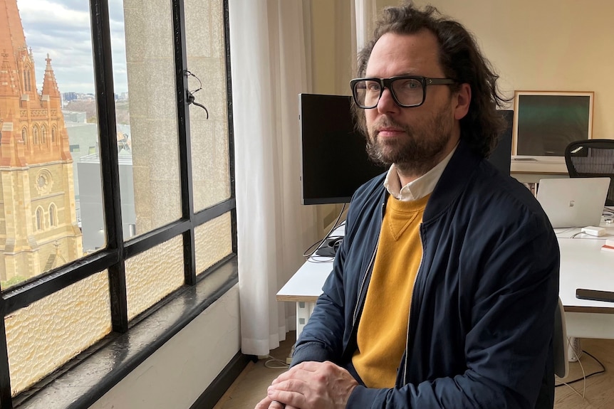 Book designer Stuart Geddes posing next to a window inside the Nicholas Building.