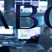 ABC logo on glass window with TV monitors in background.