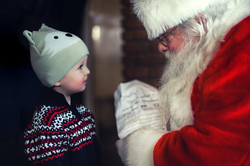 A man dressed as Santa presents a gift to a young boy.