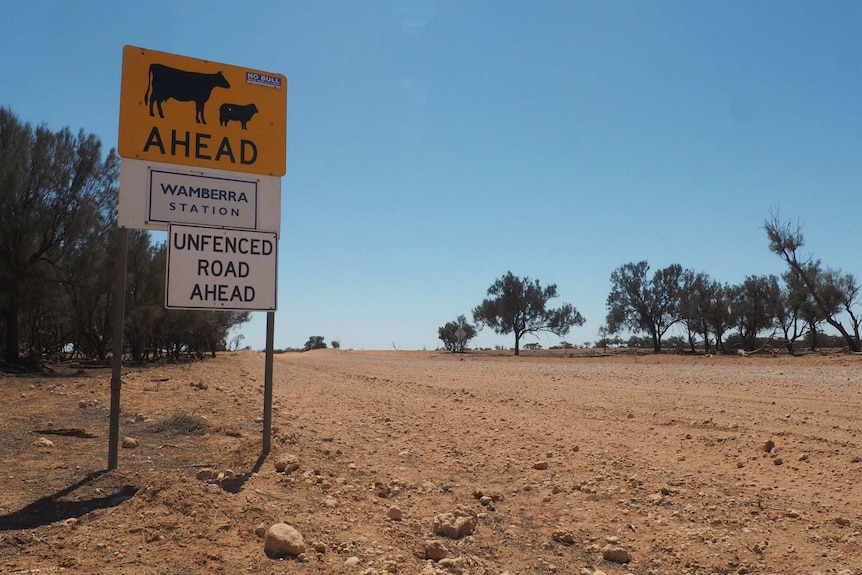 A road sign with 'stock ahead, Wamberra Station, unfenced road ahead' next to a very dry, wide dirt road.