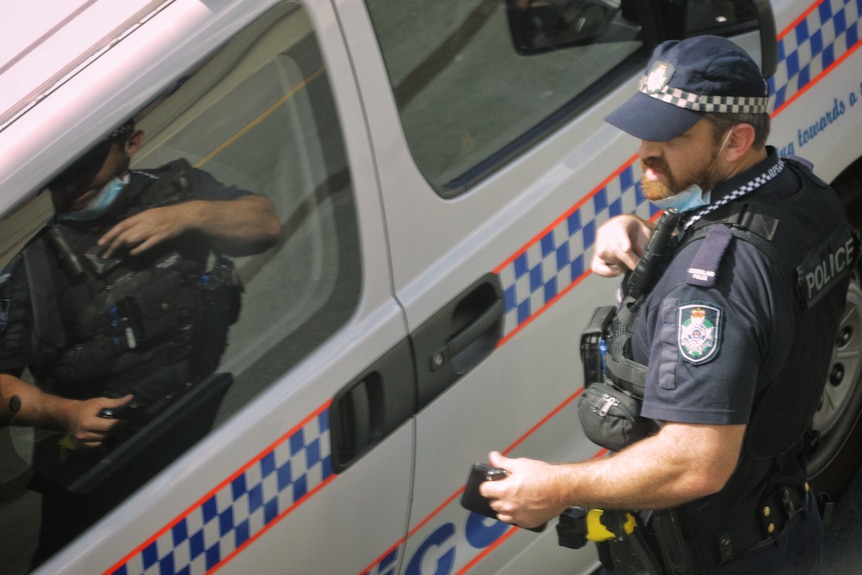 A Queensland police officer stands next to a police van.