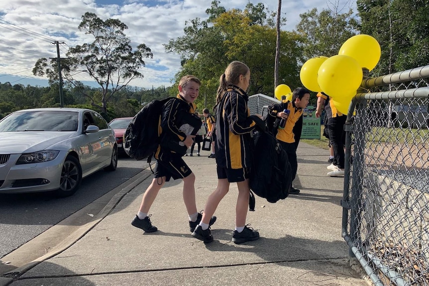 Children laughing as they walk through the front gate of a school