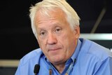 Charlie Whiting over a microphone at a press conference.